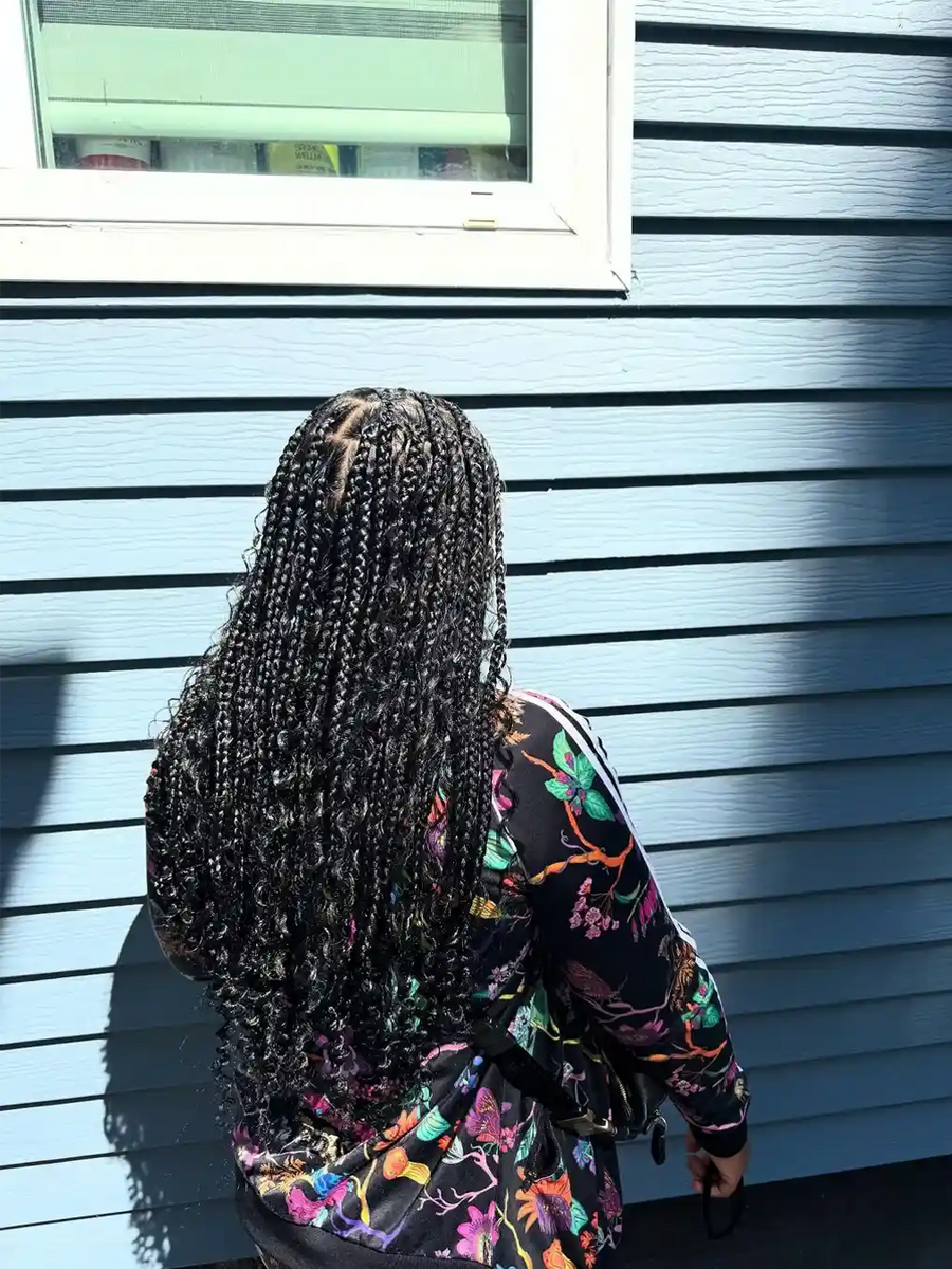 Person with braided hair standing against a blue wall