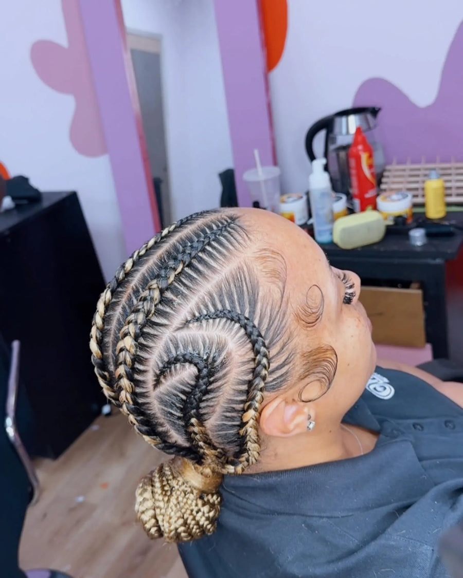 Swirl feed-in cornrows with blonde highlights styled into a low braided bun, hairstylist in Memphis, TN