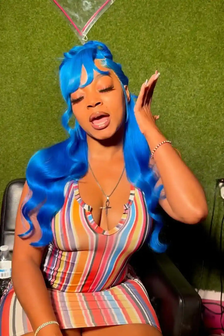 Person with blue hair wearing a colorful striped dress against a green background