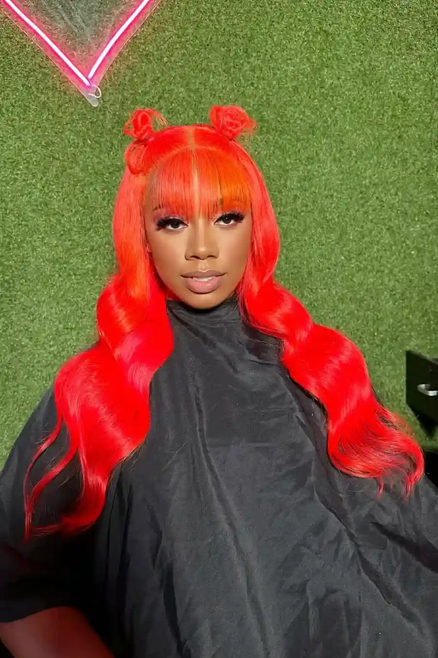 Person with bright red hair styled in twin buns against a green background