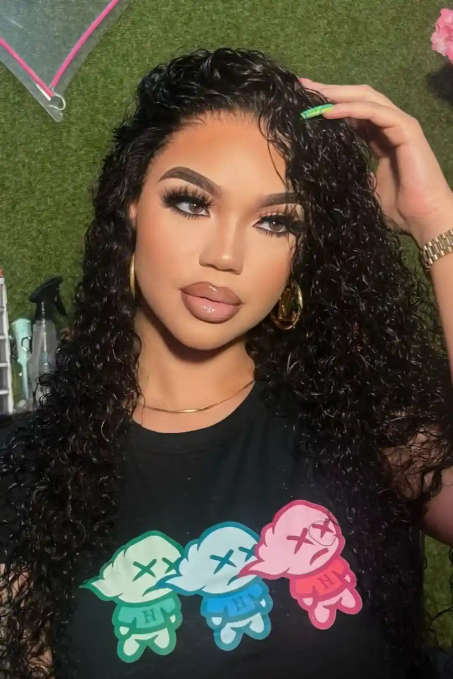 Woman with styled hair wearing a black t-shirt with colorful graphics against a green background