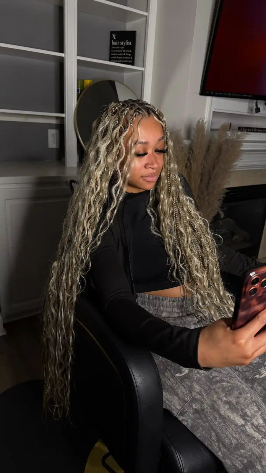 Woman with long blonde hair sitting in a chair, looking at her phone in a room.