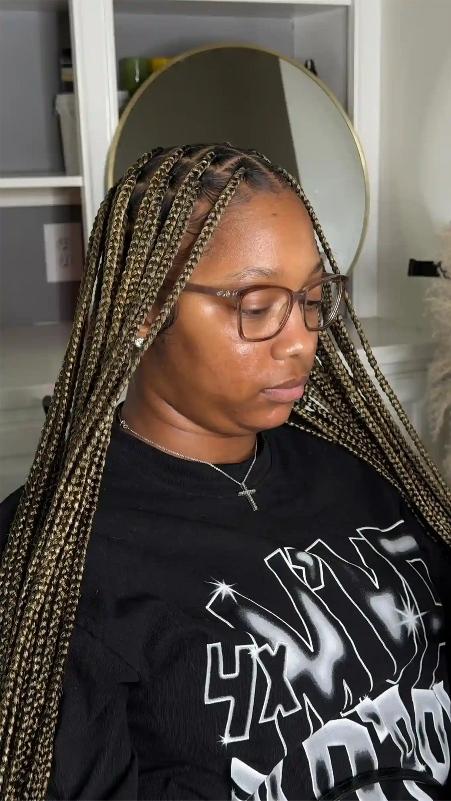Person with braided hair wearing glasses and a black shirt with white text.