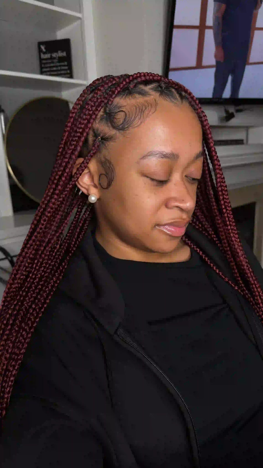 Woman with braided hair sitting in a room with a television in the background