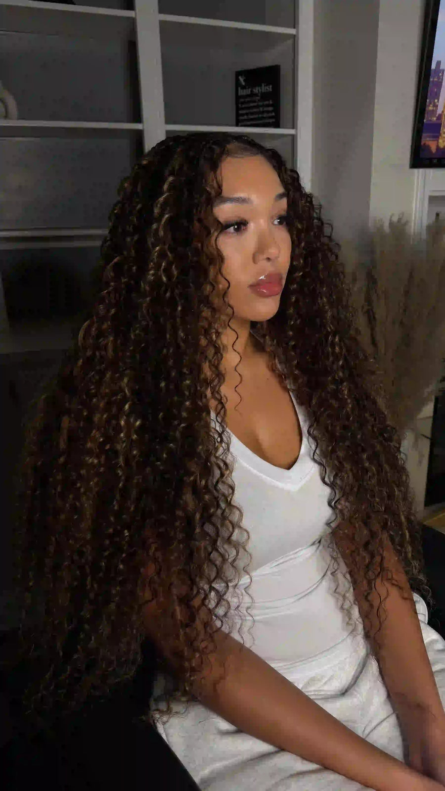 Woman with long, curly hair wearing a white top in an indoor setting.
