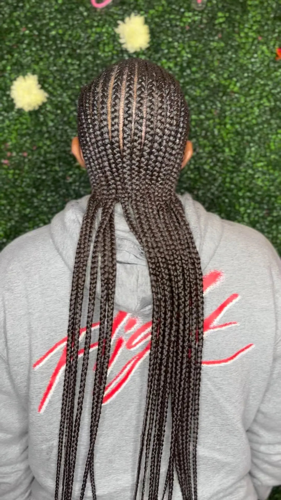 Person with braided hair wearing a gray hoodie with red text against a green textured background