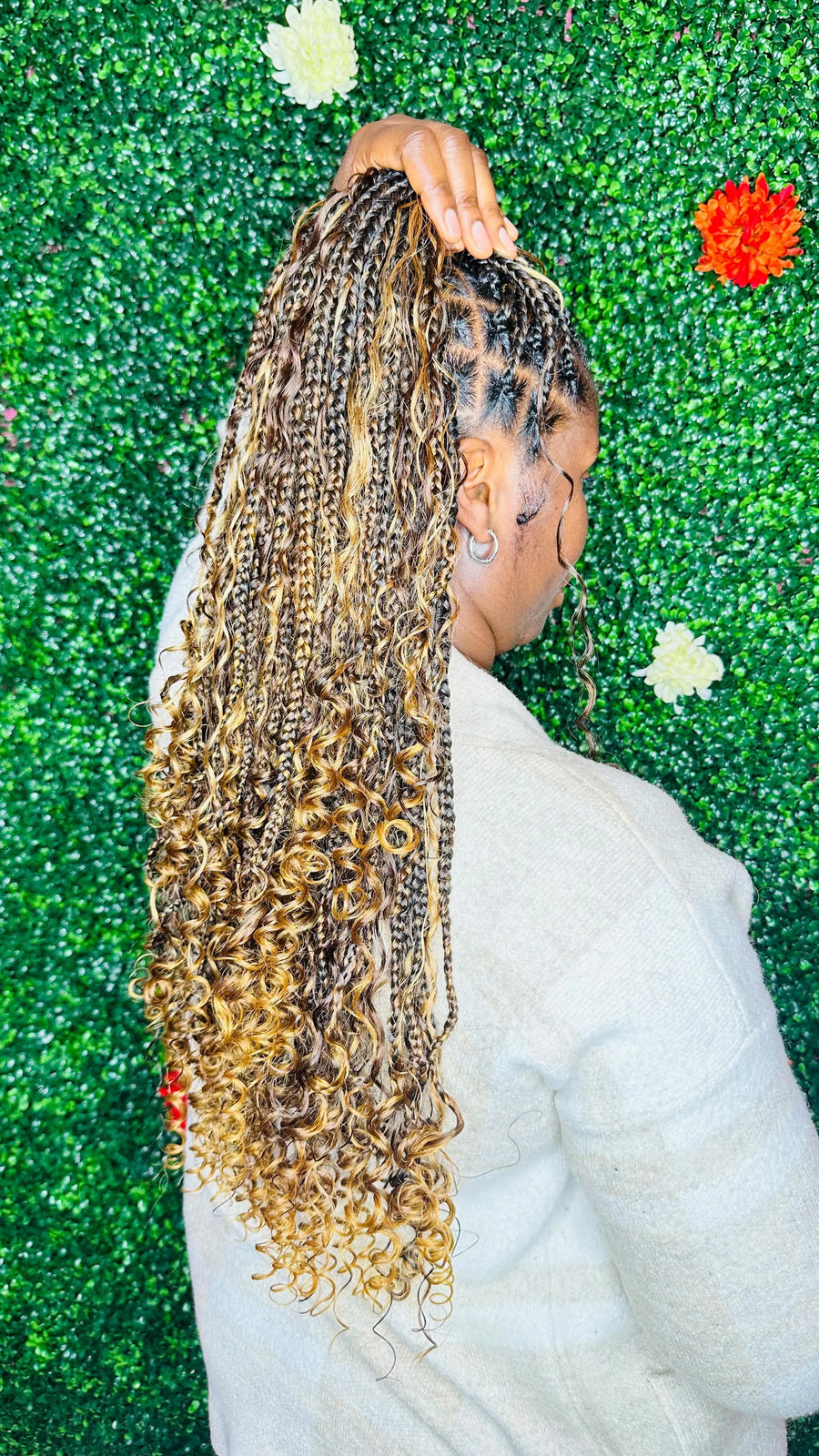 Person with braided hair against a textured green wall with flowers.