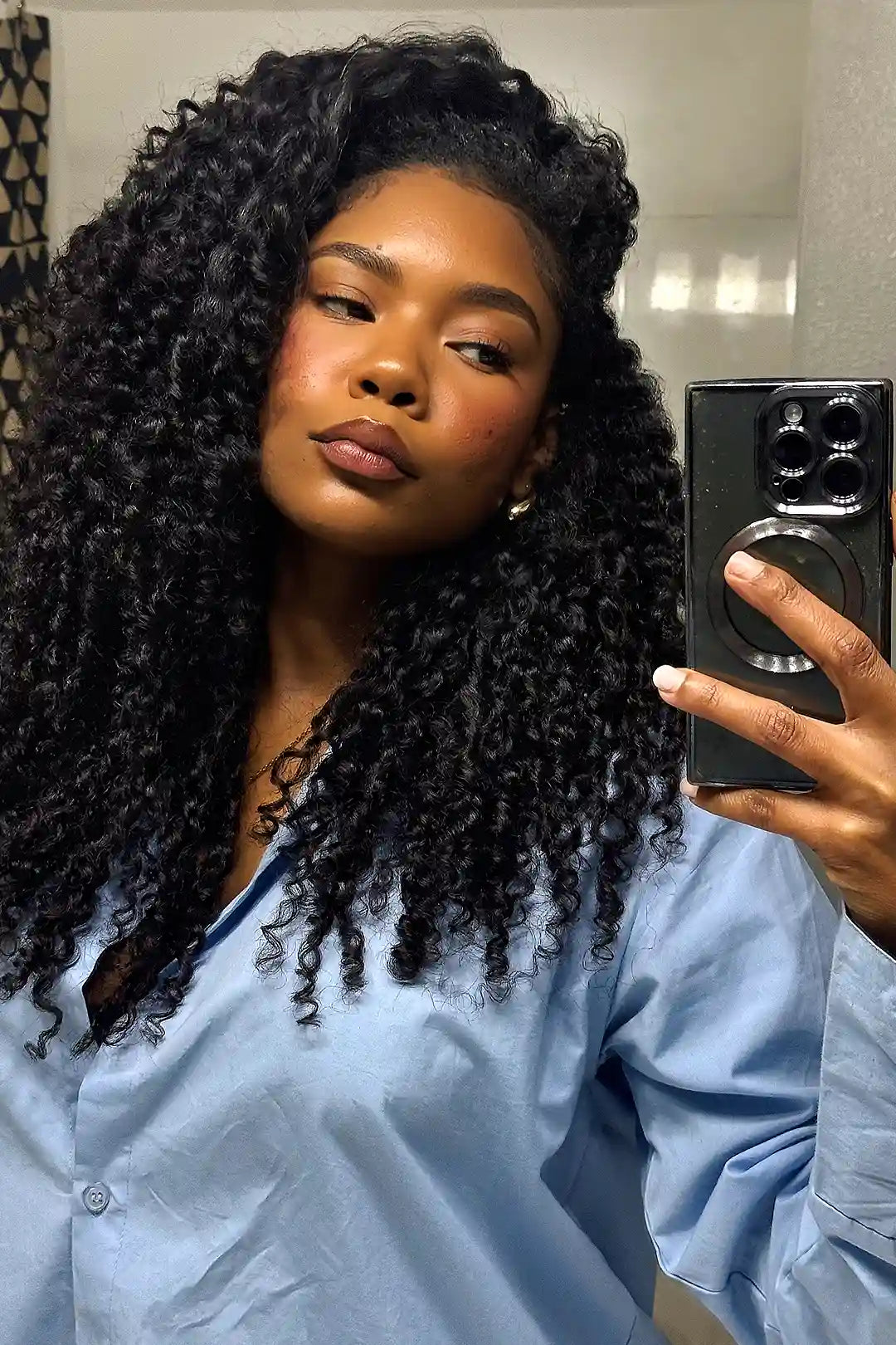 Voluminous black spiral curly feather crochet hair, double-drawn for fullness, modeled by a Black woman wearing a light blue shirt.