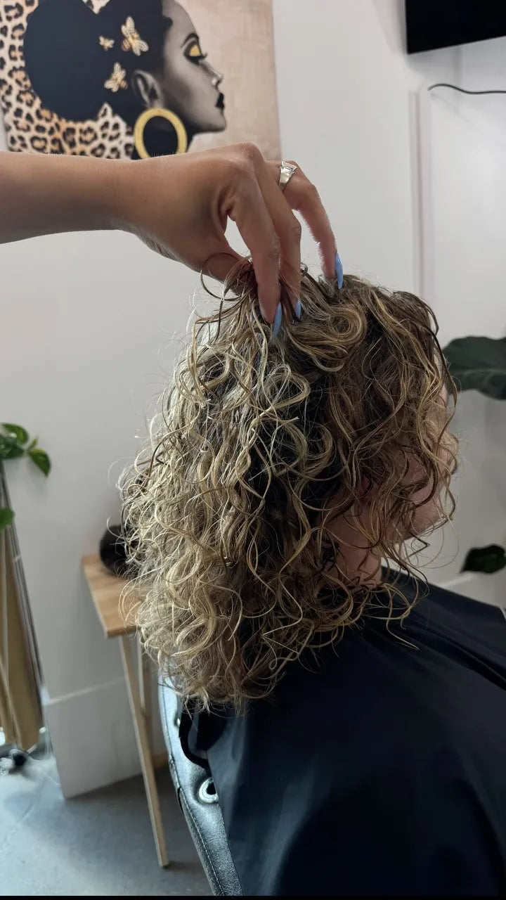 Shoulder-length blonde highlighted curly hairstyle with dimensional color and defined loose curls, Stylist located in Gilbert, AZ