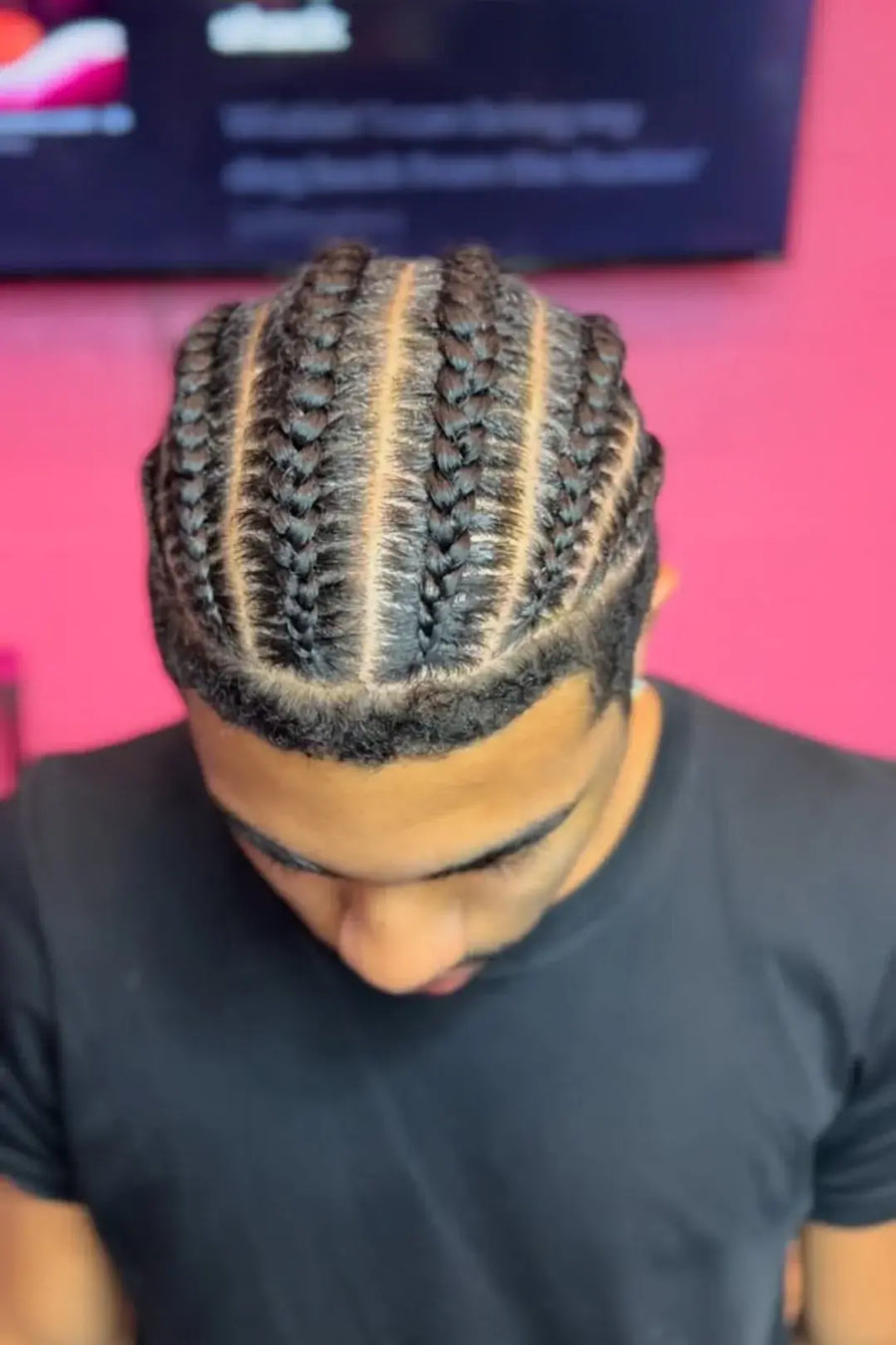 Person with braided hair wearing a black shirt against a pink background