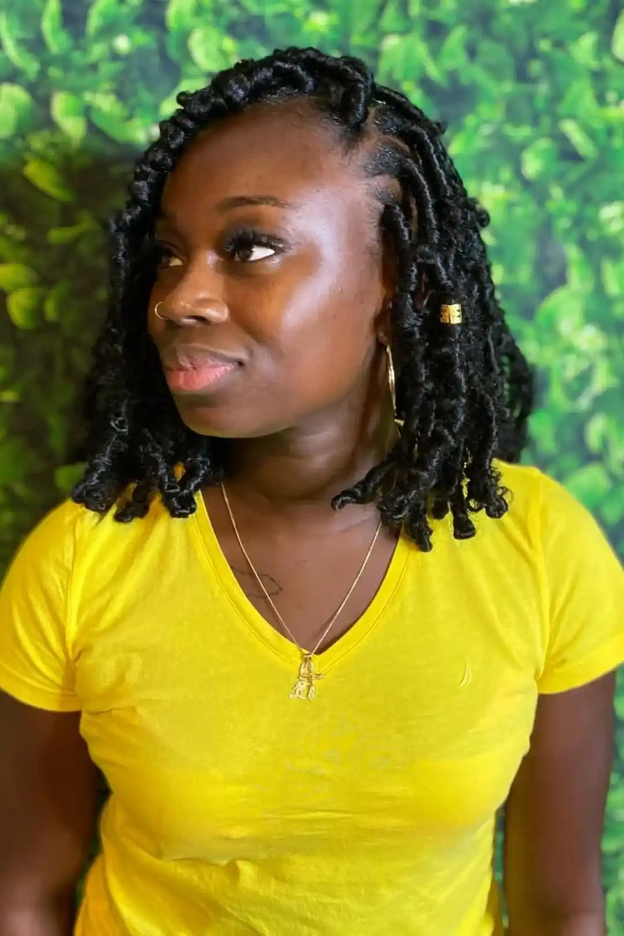 Woman with braided hair wearing a yellow shirt against a green leafy background