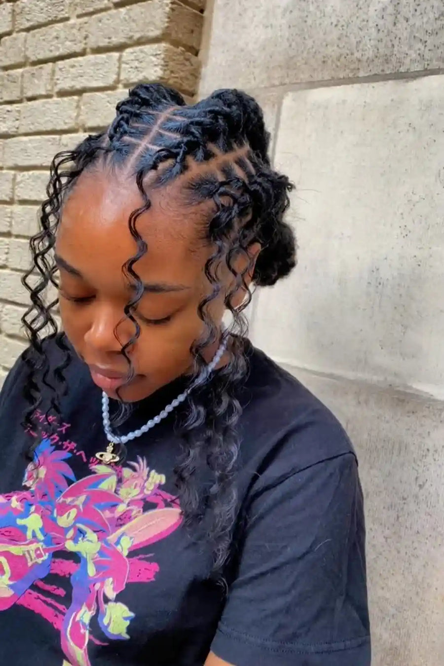 Person with styled hair sitting against a stone wall