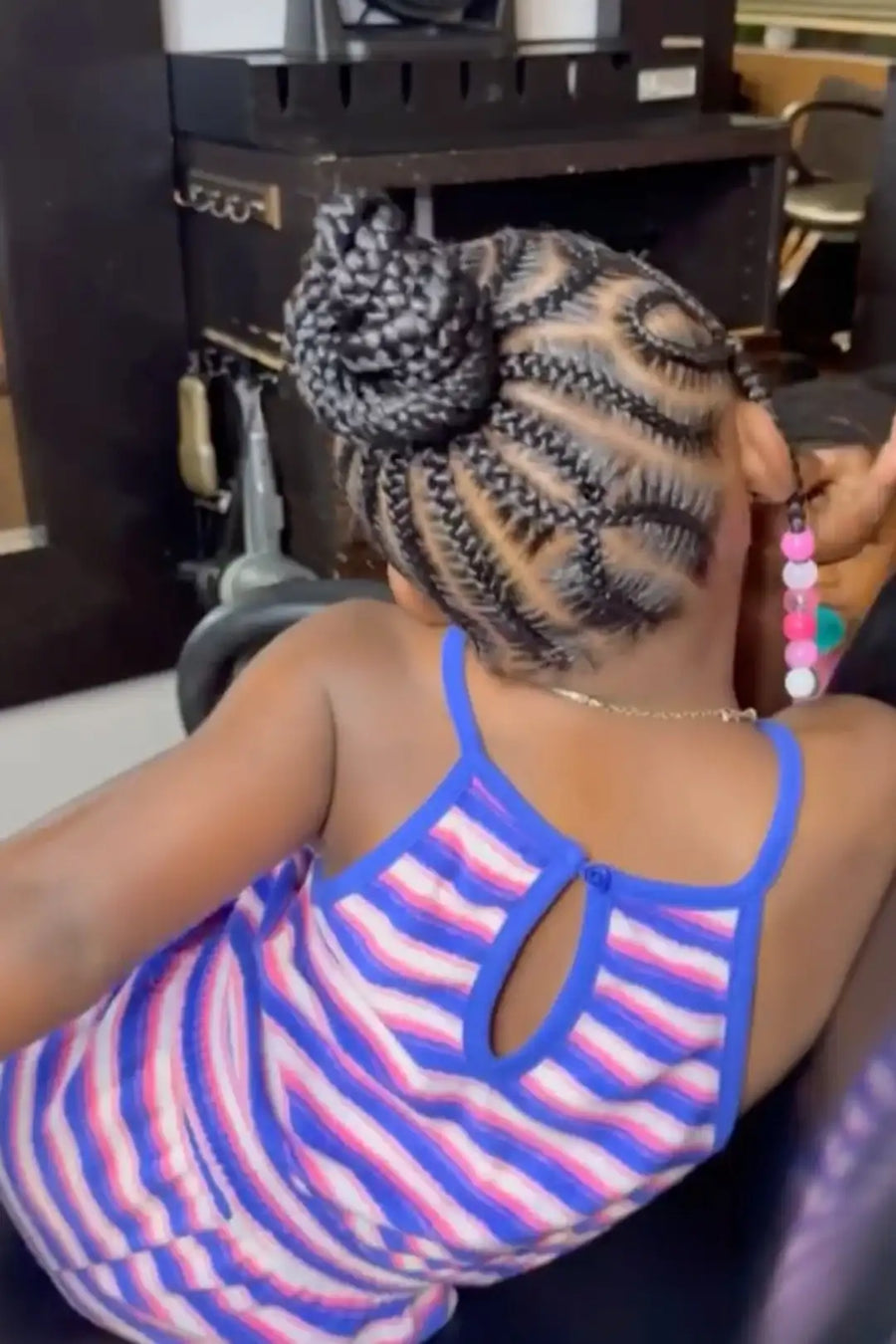 Person with braided hair sitting in a chair, wearing a colorful striped tank top.