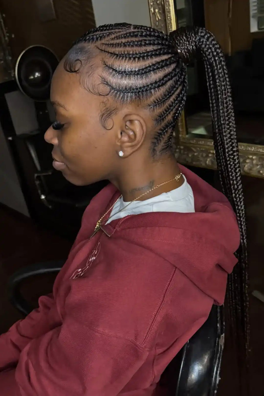 Person with braided hair wearing a red hoodie in a salon setting